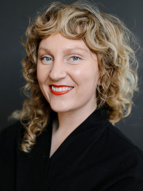 Smiling woman with curly blonde hair and red lipstick.
