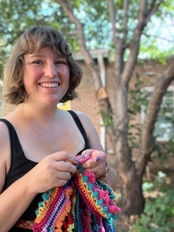 Smiling woman knitting outdoors wearing a black top.