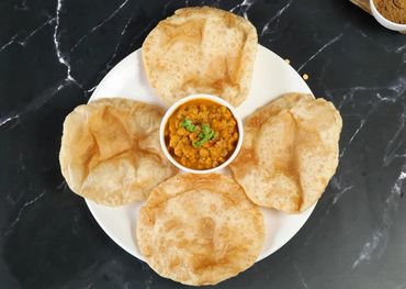 Plate of four puris with chickpea curry in the center on a white plate.