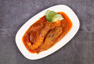 A dish of prawns in spicy red curry sauce with sliced cucumber garnish.