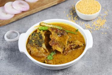A bowl of spicy fish curry garnished with green chili and coriander.