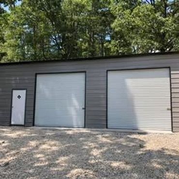Metal garage with two large roll-up doors and a side entry door.