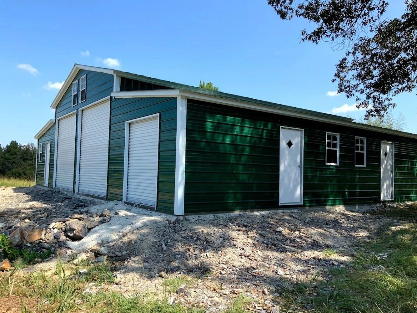 Green metal building with white doors and windows on rocky ground.