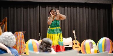 A woman in a colorful dress performing on stage with beach balls and a guitar nearby.