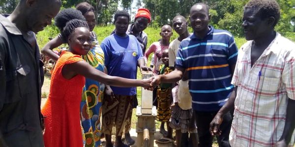 Community members shaking hands near a hand water pump.