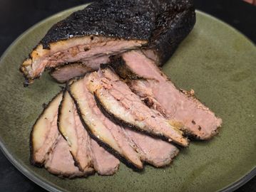 Sliced smoked brisket with a dark bark on a green plate.