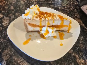 Slice of cheesecake with caramel drizzle and whipped cream on a white plate.