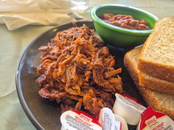 Pulled pork with baked beans, bread, and butter packets on a plate.