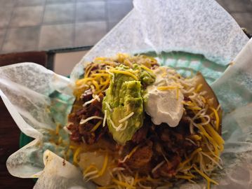 Close-up of a taco with shredded cheese, guacamole, and sour cream.