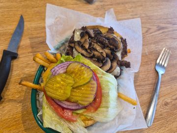 A mushroom cheeseburger with lettuce, pickles, tomato, and onions, served with fries.