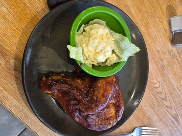 Barbecue chicken with potato salad on a black plate.