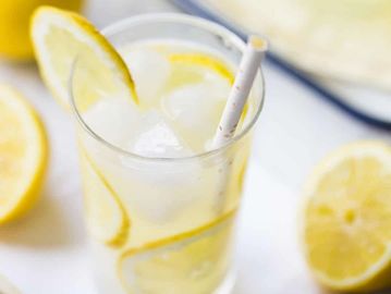 A glass of lemon water with ice and a straw.