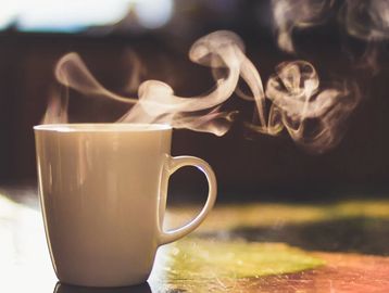 Steaming hot cup of coffee in a white mug with a blurred background.