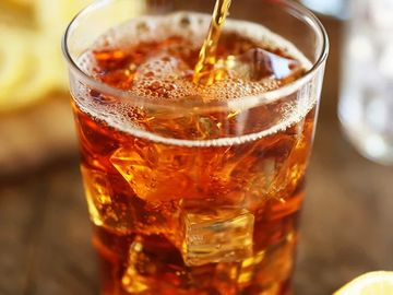 A glass of iced tea being poured with lemon nearby.