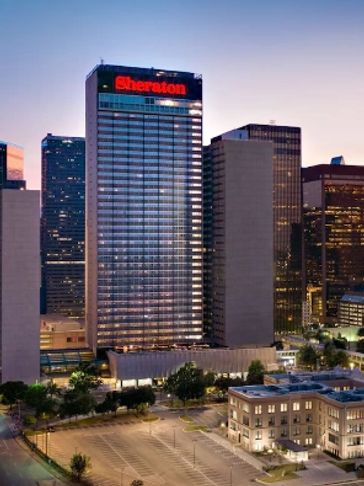 City skyline during sunset with illuminated buildings including Sheraton hotel.