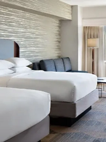 Modern hotel room with two beds and a city view.