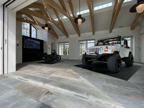 Spacious garage with a white Jeep and motorcycle under wooden beam ceiling.