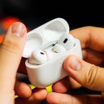 Hands holding white wireless earbuds and charging case.
