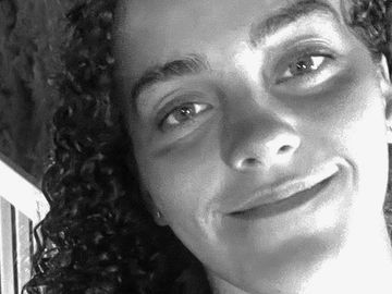 Close-up black and white portrait of a smiling person with curly hair.