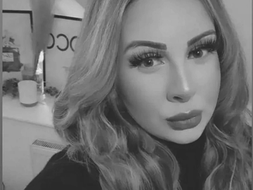 Black and white close-up selfie of a woman with styled hair and bold makeup.