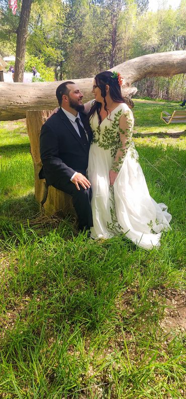 Bride and groom sit on a log for a moment whispering sweet intimate words in the forest.