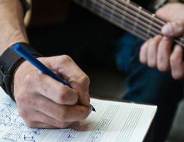 Person writing music notes while holding a guitar.