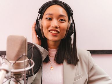 Woman recording in studio with headphones and microphone.