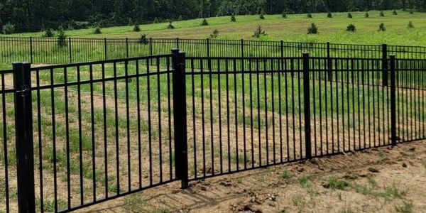 Black metal fence enclosing a grassy field with trees in the background.