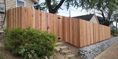 A six foot tall cedar privacy fence with a gate going down a sloped yard next to concrete steps