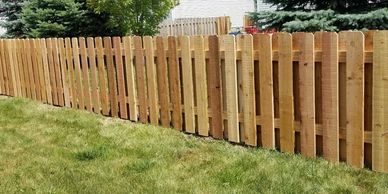A four foot tall cedar shadow box fence with a green grass yard with a pine tree behind the fence