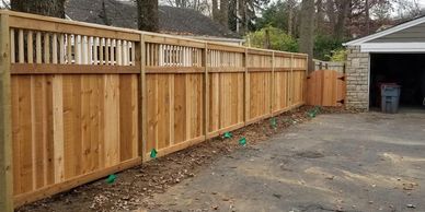 A six foot tall cedar cap and trim fence with lattice going along a driveway with a gate