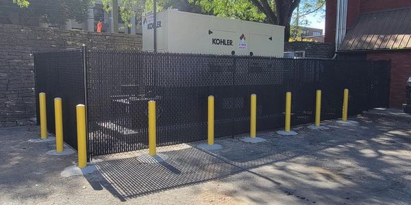 A fenced area with yellow bollards surrounding a Kohler industrial generator.