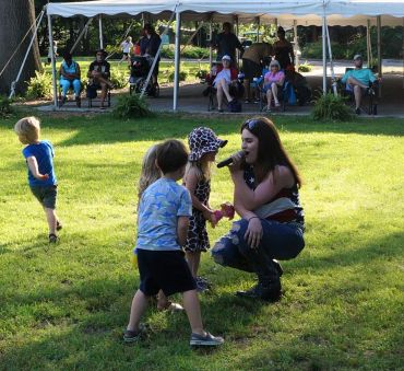 Woman singing to children at an outdoor event.