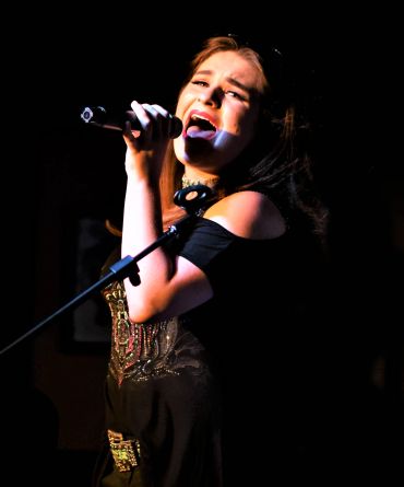 Woman singing passionately into microphone on stage.