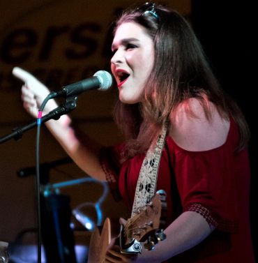 Woman singing and playing guitar on stage.