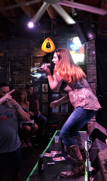 A woman singing energetically on stage at a bar.