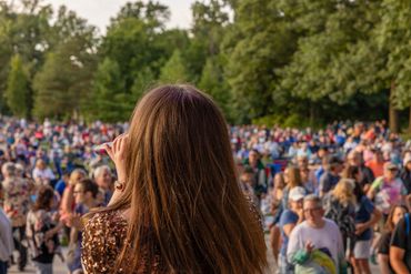 Woman singing to a large outdoor crowd.