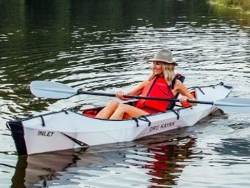 A woman kayaking on calm water wearing a red life jacket.
