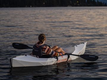 Person relaxing in a white kayak on calm water during sunset.