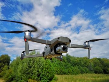 A drone flying over a green field under a blue sky with clouds.
