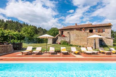 Sun loungers by a pool in front of a stone house.