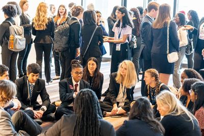 Young professionals networking at a conference, some seated in a circle and others standing.