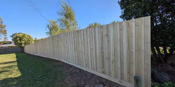 New wooden fence stretching along a backyard under clear sky.