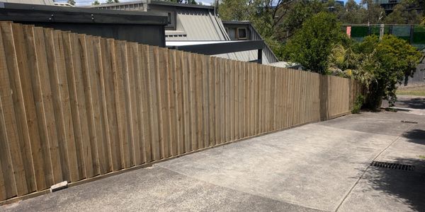 A long wooden fence along a concrete driveway on a sunny day.