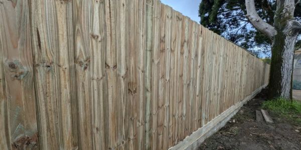A long wooden fence with a concrete base beside a tree.