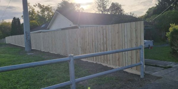 A newly installed wooden fence extends along a residential property during sunset.