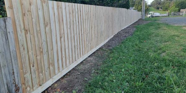 A long wooden fence alongside a grassy area and dirt path.