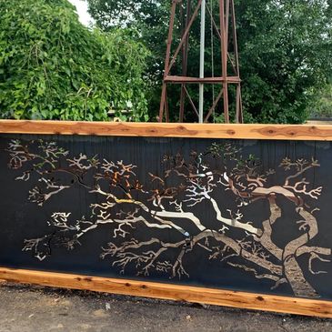 Metal tree art on a wooden frame gate outdoors.