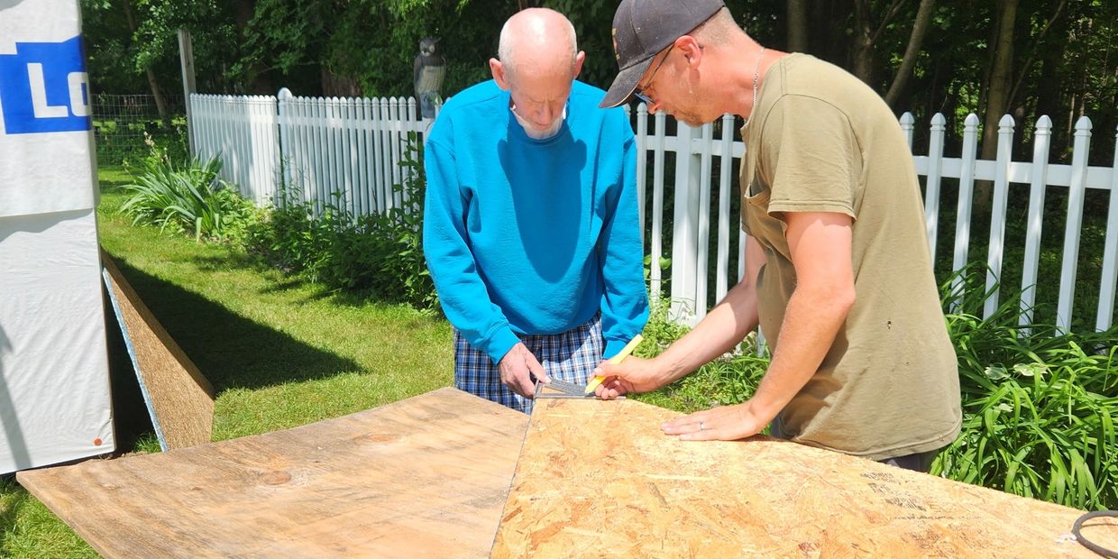 Two men measuring and marking wood outdoors for a construction project.