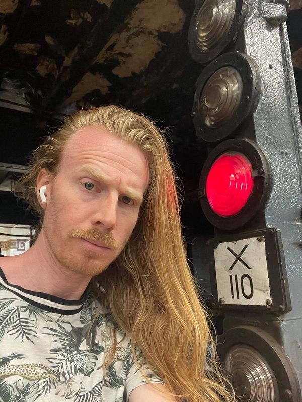 Mercury with mustache, white male w/ red strawberry hair next to stop lights for train, forest shirt